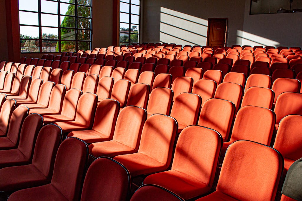 A sunlit, empty auditorium displaying rows of red chairs and shadow patterns.