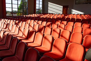 A sunlit, empty auditorium displaying rows of red chairs and shadow patterns.
